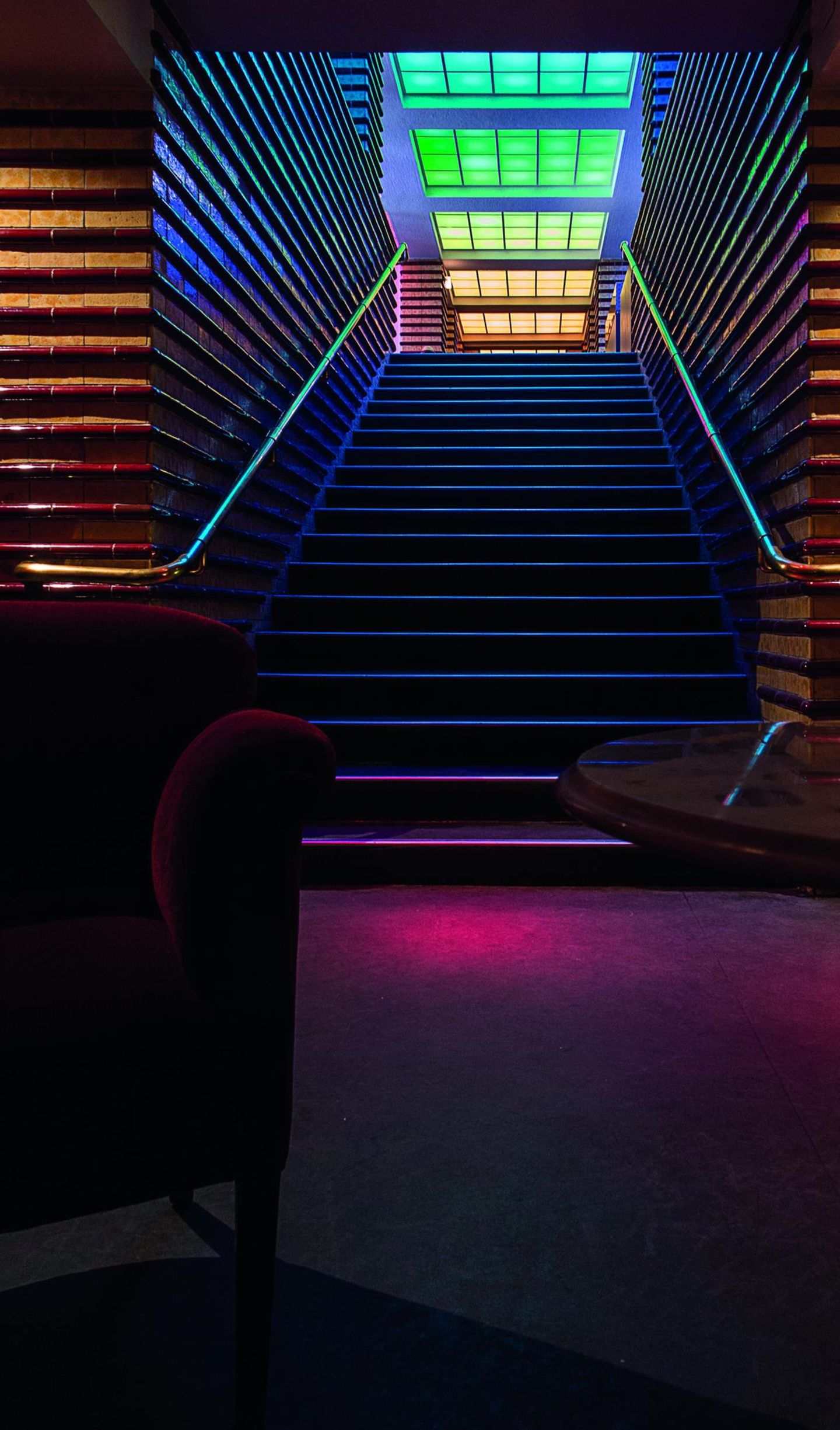 Roter Vorhang: das Rabenhof Theater Bunt beleuchtete Treppe mit buntem Glas, es ist sehr dunkel.