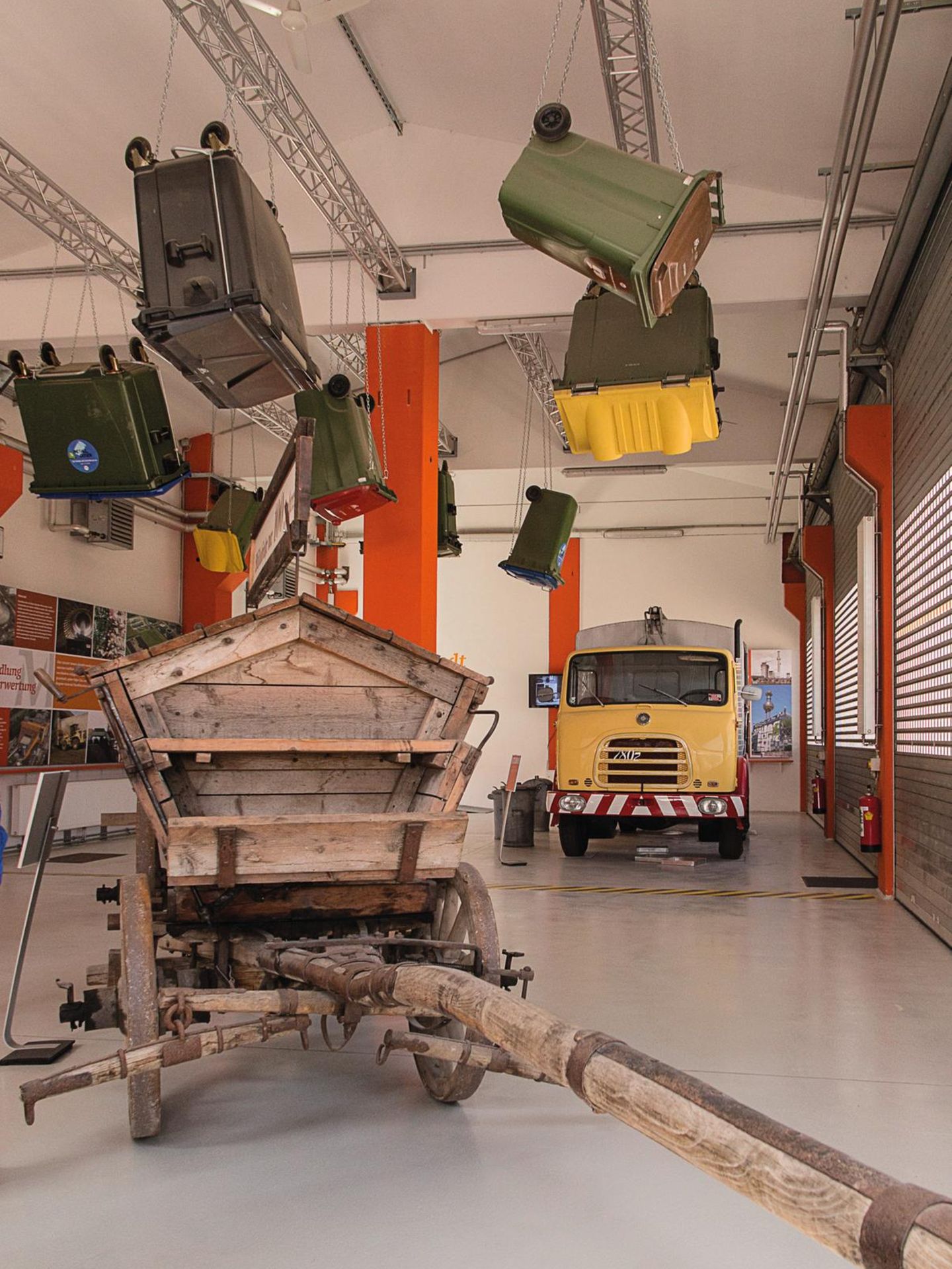Trash Art: das Müllmuseum Müllauto und Mistkarren in einem großen Raum, Mülltonnen hängen von der Decke.