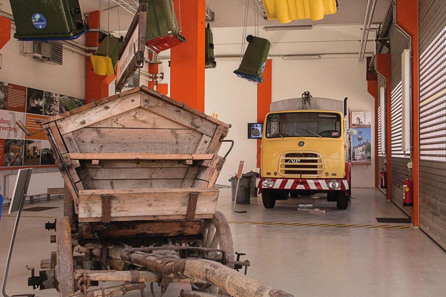 Trash Art: das Müllmuseum Müllauto und Mistkarren in einem großen Raum, Mülltonnen hängen von der Decke.