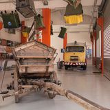 Müllauto und Mistkarren in einem großen Raum, Mülltonnen hängen von der Decke.