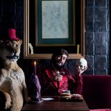 Viktor Wynd im Samtjacket sitzt auf einem Sofa, in der Hand ein Totenschädel. Daneben steht ein ausgestopfter Löwe.