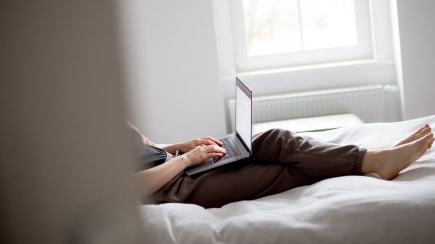 Eine Person liegt mit Laptop und Jogginghose auf einem Bett. Das Gesicht ist nicht erkennbar Eine Person liegt mit Laptop und Jogginghose auf einem Bett. Das Gesicht ist nicht erkennbar