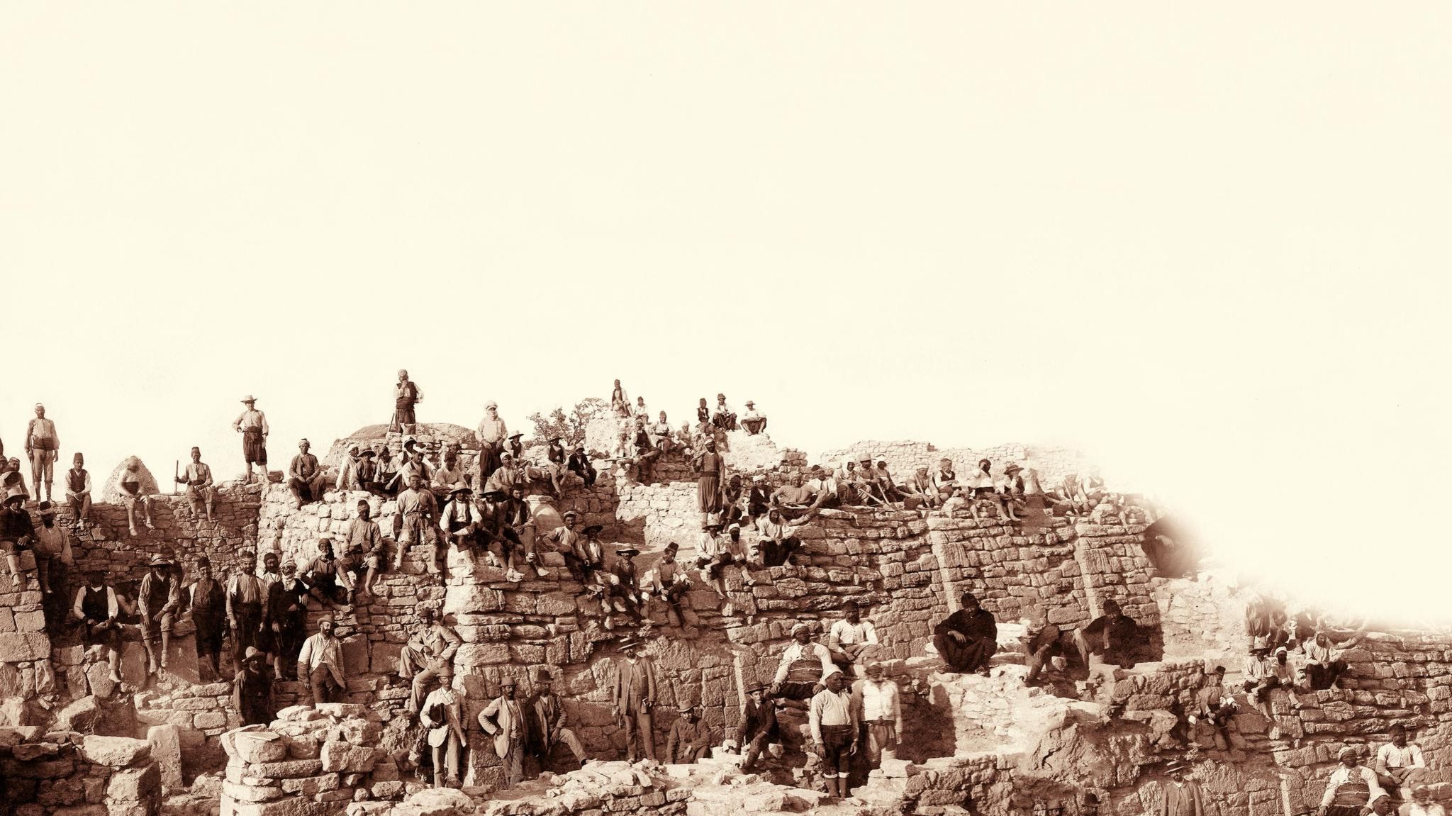 Männer in Anzügen und orientalischer Arbeitskleidung posieren auf einem Ruinenhügel in der heutigen Türkei, schwarz-weiß Foto