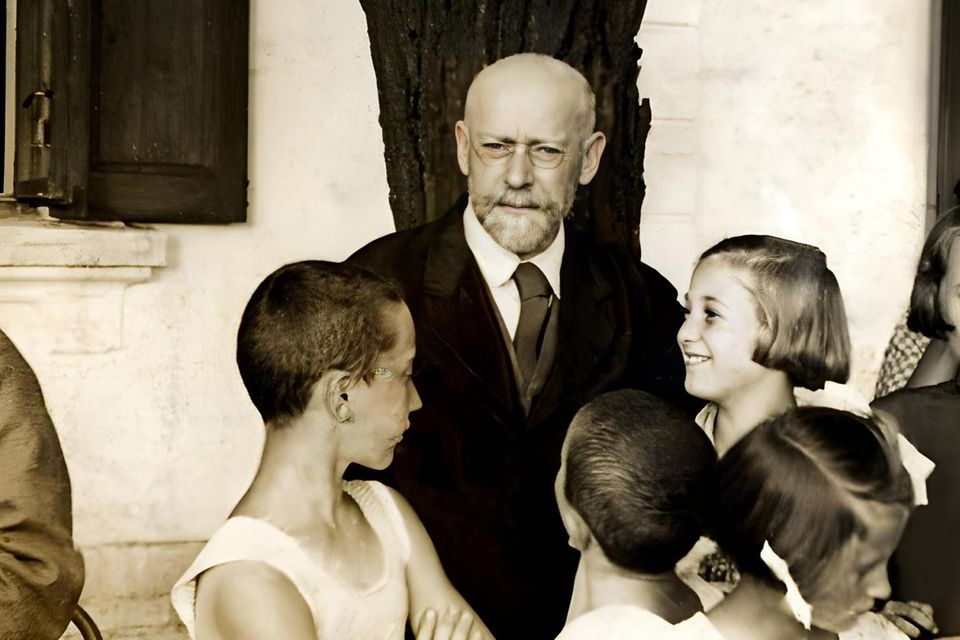 Janusz Korczak, ein älterer Mann mit Bart und Brille, wird von mehreren Kindern umringt