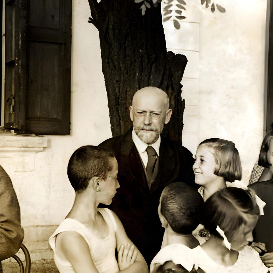 Janusz Korczak, ein älterer Mann mit Bart und Brille, wird von mehreren Kindern umringt Janusz Korczak, ein älterer Mann mit Bart und Brille, wird von mehreren Kindern umringt