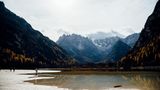 Bewaldete Hänge,  unten ein See mit Kiesbänken. Darauf steht ein Mensch.