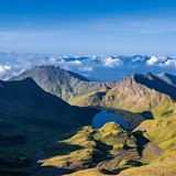 Kahles felsiges Hochgebirge, in der Senke liegt ein See. Blick geht weit in die Wolken.