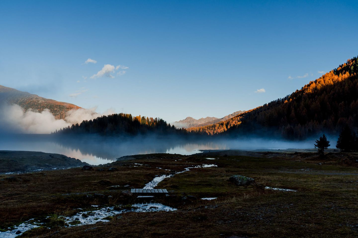 Morgennebel am noch dunklen See, erstes Licht auf den Bergspitzen.