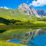 Schroffer Felsgipfel, darunter Almgürtel mit Häusern, alles spiegelt sich im See.