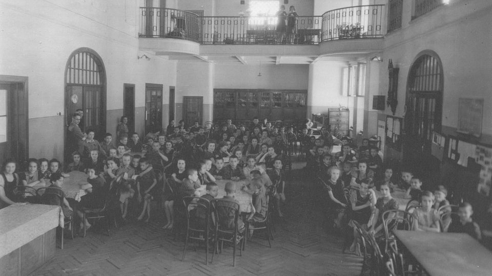 Mehrere Dutzend Waisenkinder sitzen in einem hohen Saal im Warschauer Waisenhaus von Janusz Korczak