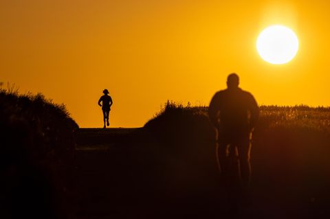 Joggerin und Radfahrer im Gegenlicht bei Sonnenaufgang