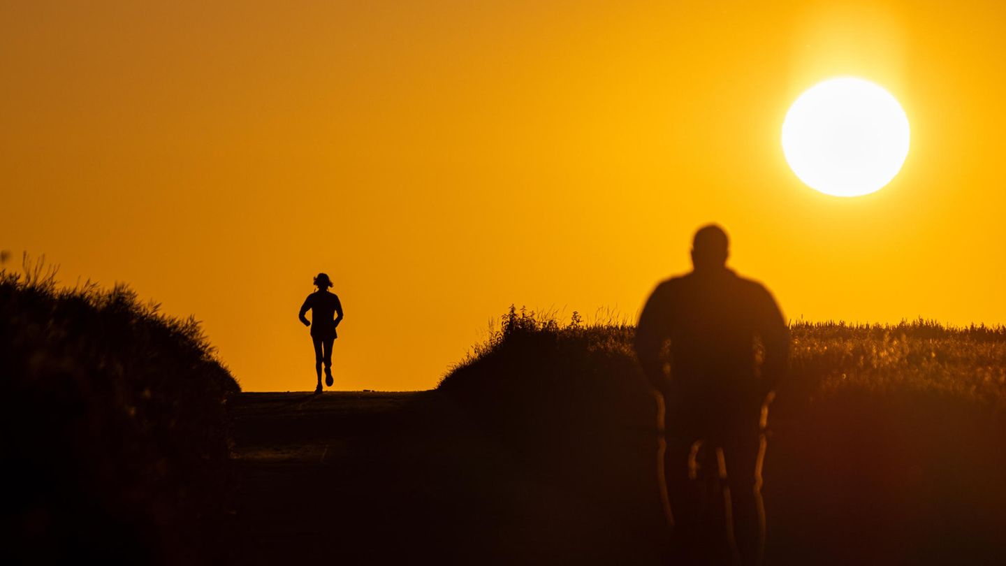 Joggerin und Radfahrer im Gegenlicht bei Sonnenaufgang