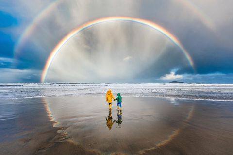 Zwei Kinder am Strand unter einem kompletten Regenbogen