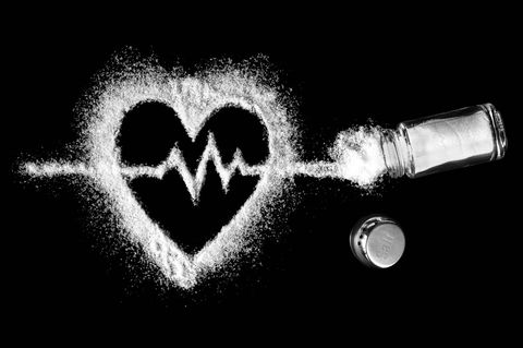 Ein Herz aus Salzkrümeln auf schwarzem Grund, daneben ein umgefallener Salzstreuer