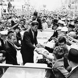 John F. Kennedy , stehend in einem offenen Auto, umringt von Anhängern mit Wahl-Plakaten; sw-Foto