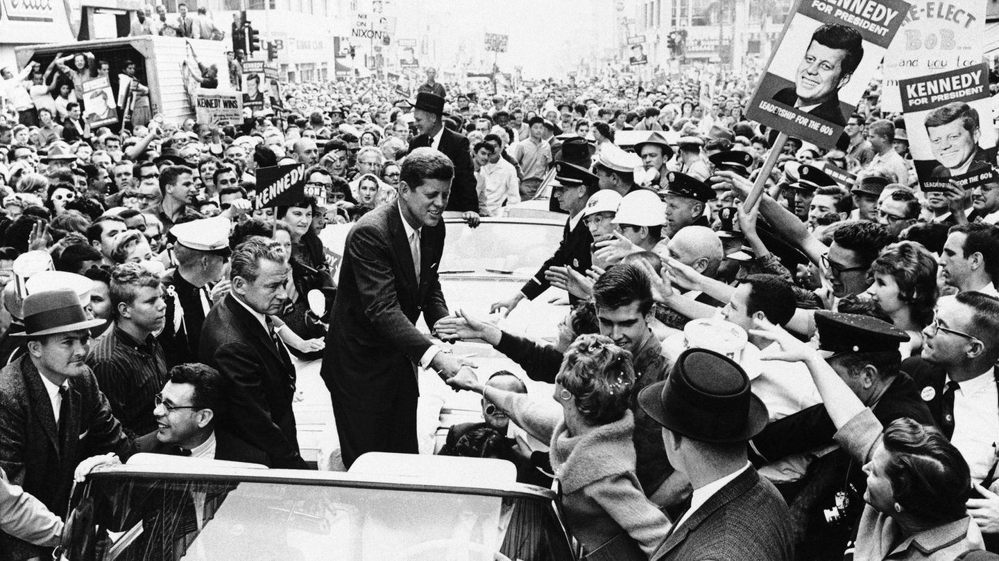 Zum Siegen erzogen John F. Kennedy , stehend in einem offenen Auto, umringt von Anhängern mit Wahl-Plakaten; sw-Foto