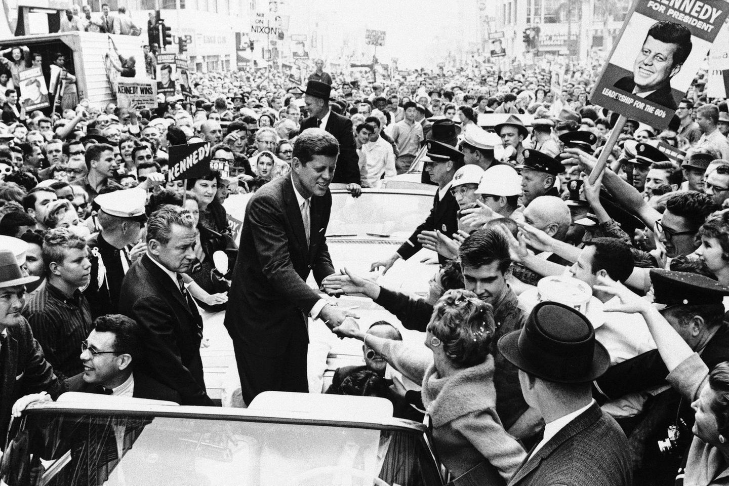 Zum Siegen erzogen John F. Kennedy , stehend in einem offenen Auto, umringt von Anhängern mit Wahl-Plakaten; sw-Foto