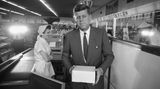 Kennedy mit einer Pappschachtel in der Hand in einem Lebensmittelgeschäft; sw-Foto