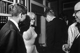 Marilyn Monroe in einem hautengen Kleid, Kennedy und andere stehen vor einer Bücherwand zusammen; sw-Foto