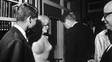 Marilyn Monroe in einem hautengen Kleid, Kennedy und andere stehen vor einer Bücherwand zusammen; sw-Foto