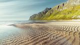 Am Ersfjord-Strand sorgt die Brandung dafür, dass die Wellen auch jenseits des Spülsaumes weitergehen. Umgeben von hohen, steilen Gipfeln entsteht hier eine skandinavische Karibikkulisse. Sie liegt direkt an der beliebten Landschaftsroute 862 auf der Insel Senja