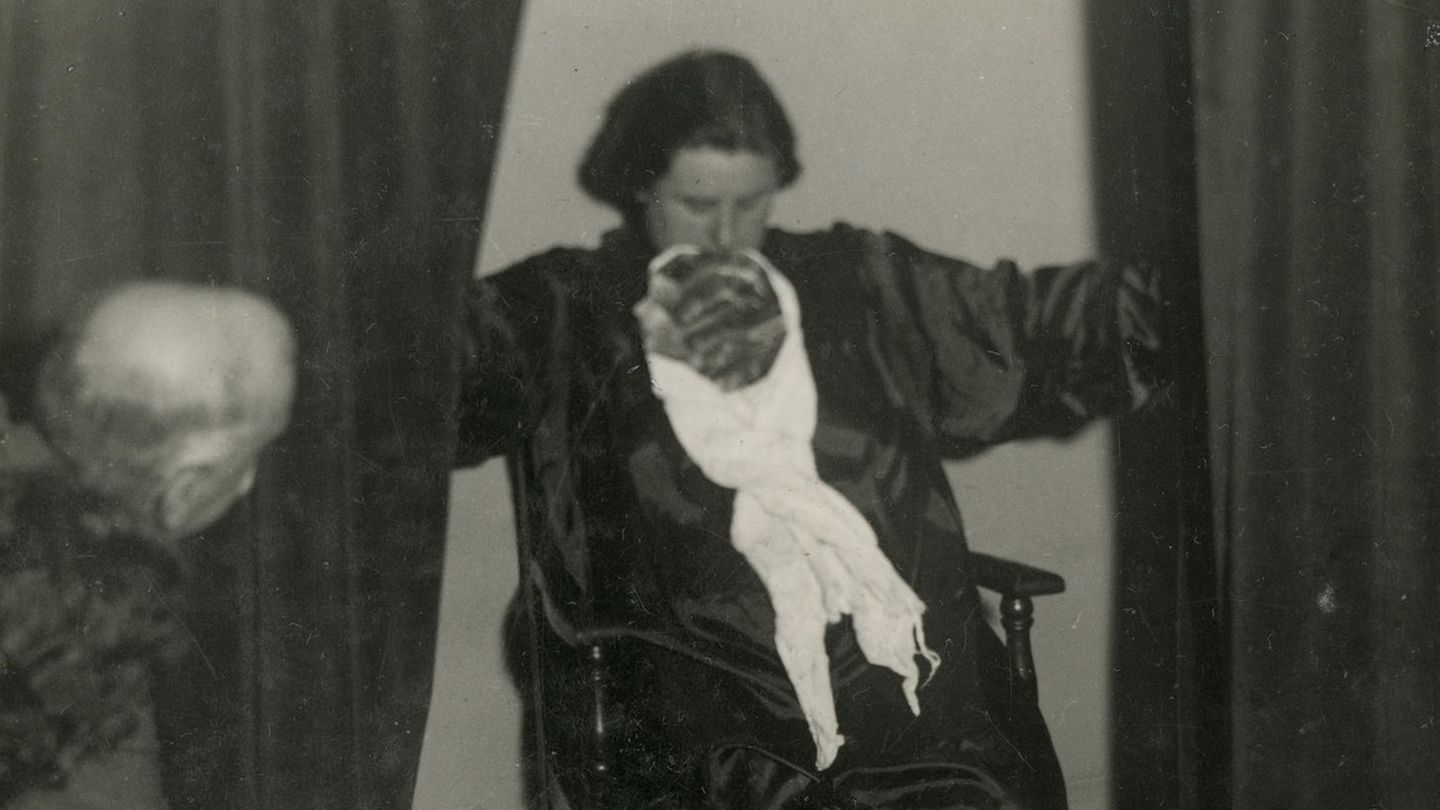 Helen Duncan sitzt auf einem Stuhl und würgt Tücher aus dem Mund