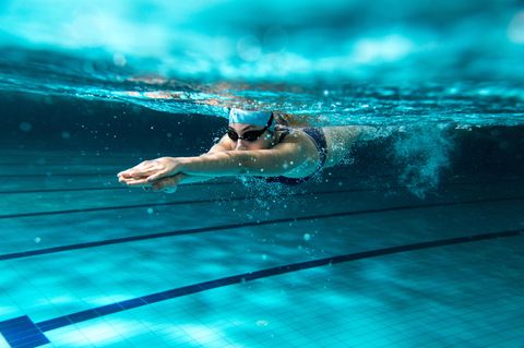 Frau schwimmt unterwasser mit Badekappe und Schwimmbrille