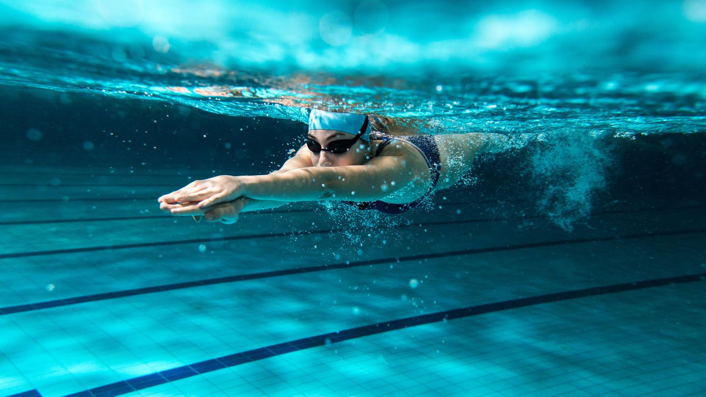 Frau schwimmt unterwasser mit Badekappe und Schwimmbrille