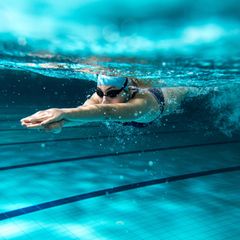Frau schwimmt unterwasser mit Badekappe und Schwimmbrille