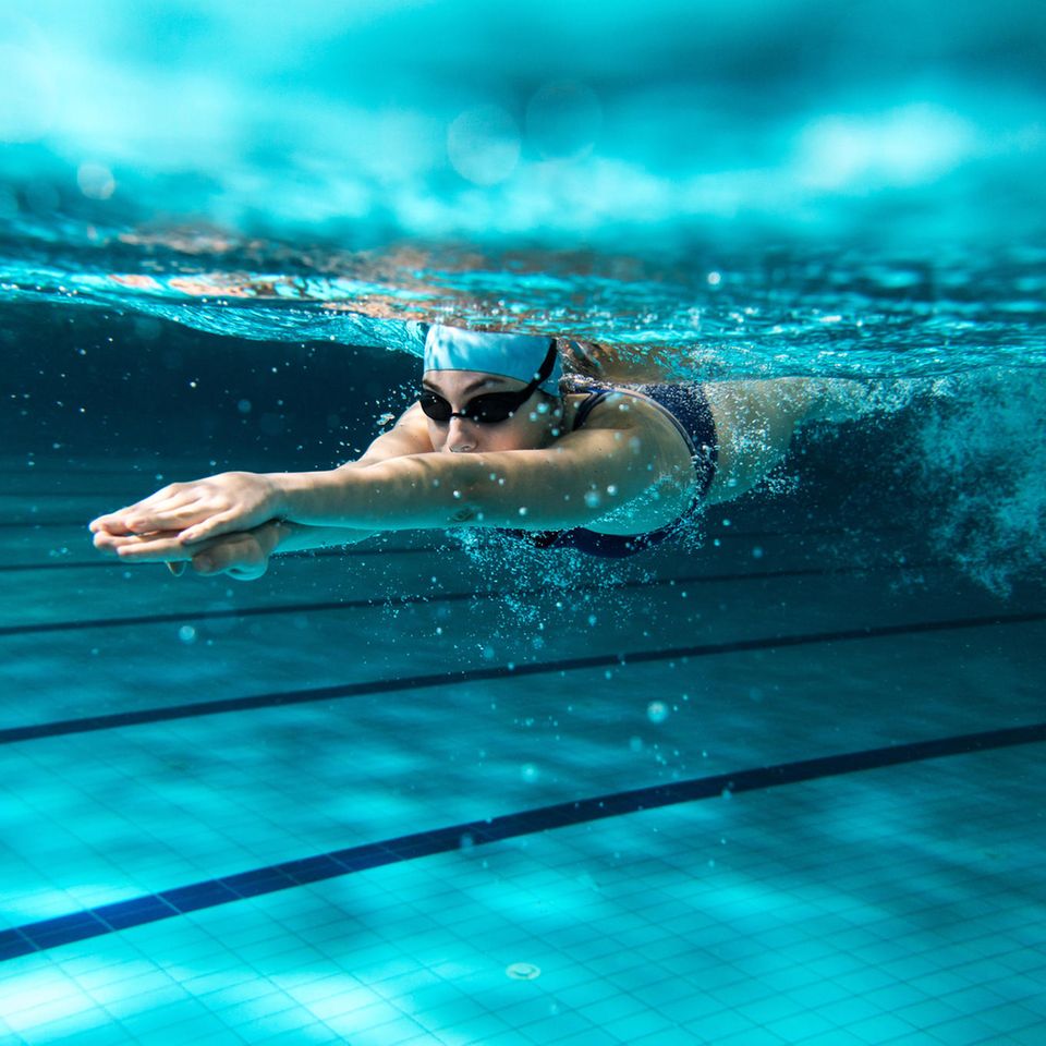 Frau schwimmt unterwasser mit Badekappe und Schwimmbrille
