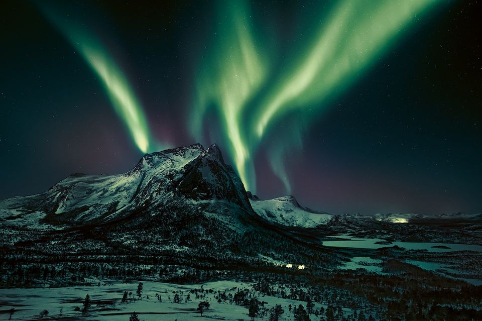 Leuchtspuren am Firmament. Eine Aurora borealis, ein Polarlicht, zaubert grünliche Streifen in den Nachthimmel. Dabei in Szene gesetzt: der Hjoerna, ein 843 Meter hoher Berg aus Granit in der Provinz Nordland im Norden Norwegens. Das geisterhafte nächtliche Spektakel kann entstehen, sobald elektrisch geladene Teilchen des Sonnenwinds auf Moleküle in der Erdatmosphäre treffen  1.4993