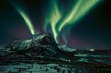 Leuchtspuren am Firmament. Eine Aurora borealis, ein Polarlicht, zaubert grünliche Streifen in den Nachthimmel. Dabei in Szene gesetzt: der Hjoerna, ein 843 Meter hoher Berg aus Granit in der Provinz Nordland im Norden Norwegens. Das geisterhafte nächtliche Spektakel kann entstehen, sobald elektrisch geladene Teilchen des Sonnenwinds auf Moleküle in der Erdatmosphäre treffen