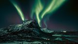 Leuchtspuren am Firmament. Eine Aurora borealis, ein Polarlicht, zaubert grünliche Streifen in den Nachthimmel. Dabei in Szene gesetzt: der Hjoerna, ein 843 Meter hoher Berg aus Granit in der Provinz Nordland im Norden Norwegens. Das geisterhafte nächtliche Spektakel kann entstehen, sobald elektrisch geladene Teilchen des Sonnenwinds auf Moleküle in der Erdatmosphäre treffen