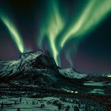 Leuchtspuren am Firmament. Eine Aurora borealis, ein Polarlicht, zaubert grünliche Streifen in den Nachthimmel. Dabei in Szene gesetzt: der Hjoerna, ein 843 Meter hoher Berg aus Granit in der Provinz Nordland im Norden Norwegens. Das geisterhafte nächtliche Spektakel kann entstehen, sobald elektrisch geladene Teilchen des Sonnenwinds auf Moleküle in der Erdatmosphäre treffen