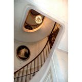 Wendeltreppe mit alten Bildern an den Wänden, moderner Kronleuchter hängt in der Mitte