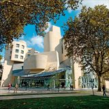 Zwischen Bäumen ragt das verschachtelte Gebäude in den klaren Himmel.