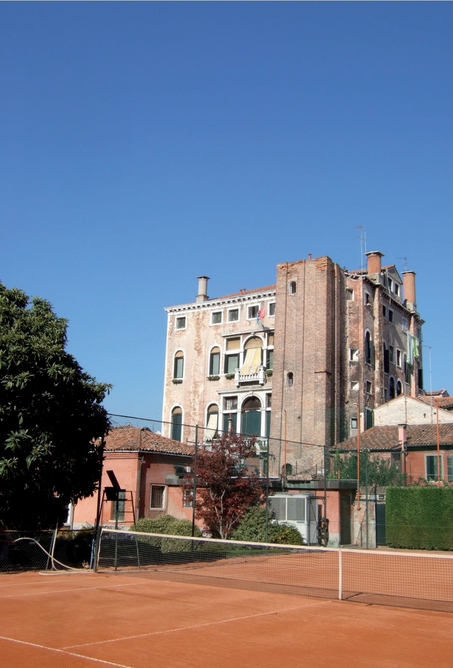 Aufschlag im Getümmel: Tennisplatz in San Polo Tennisplatz mit Aschebelag, dahinter sehr alte Häuser und ein Baum
