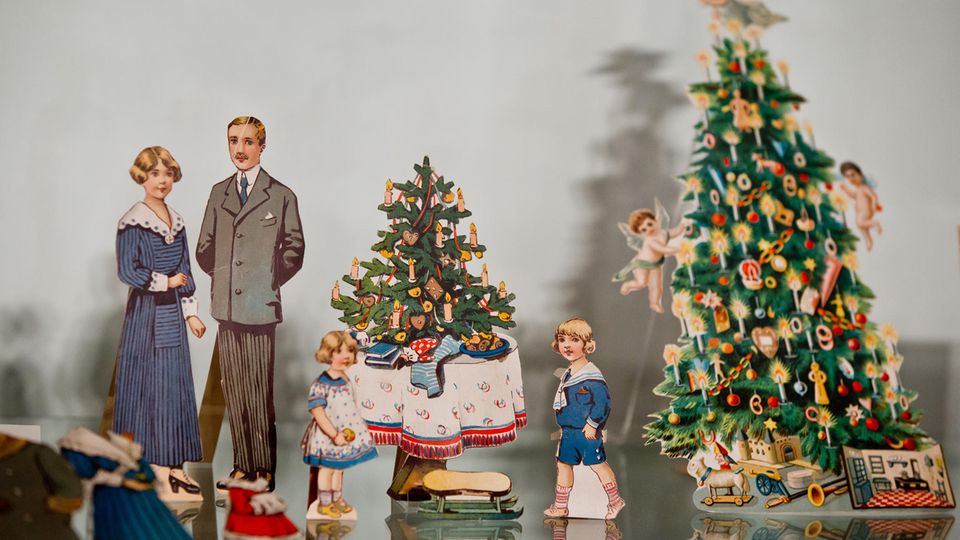 Ankleidepuppen mit Kleidungsstücken, einem Weihnachtsbaum und Geschenken (um 1920)