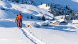Zwei Schneeschuhwandernde und Hütten im Hintergrund
