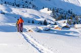 Zwei Schneeschuhwandernde und Hütten im Hintergrund