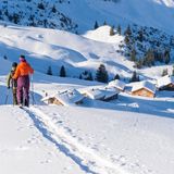 Zwei Schneeschuhwandernde und Hütten im Hintergrund