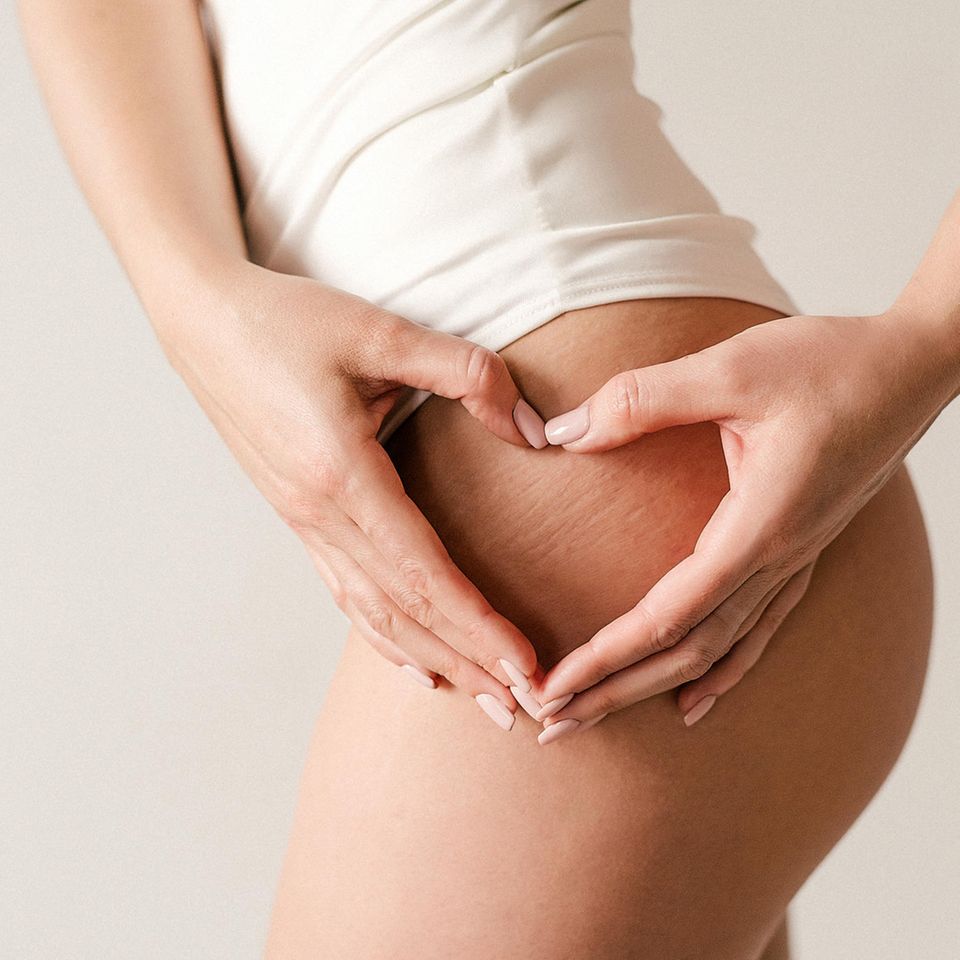 Eine Frau zeigt mit ihren Händen ein Herz auf ihrem Oberschenkel Eine Frau zeigt mit ihren Händen ein Herz auf ihrem Oberschenkel