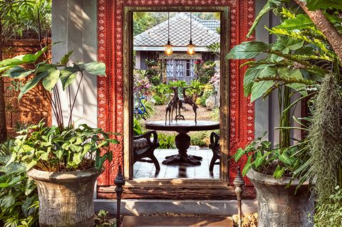 Es grünt und blüht, zwitschert und duftet und könnte der Eingang zum Paradies sein. Wenn es ein Eingang wäre: Der rote Türrahmen im »Baan Botanica« fasst einen Spiegel ein, der das gegenüberliegende Gästehaus im Privatgarten des Landschaftsarchitekten Bill Bensley zeigt. Sein rund 3200 Quadratmeter großes Refugium beherbergt 1500 tropische Pflanzenarten, Springbrunnen, Statuen, Pagoden und Pergolen. Definitiv ein menschengemachtes Paradies