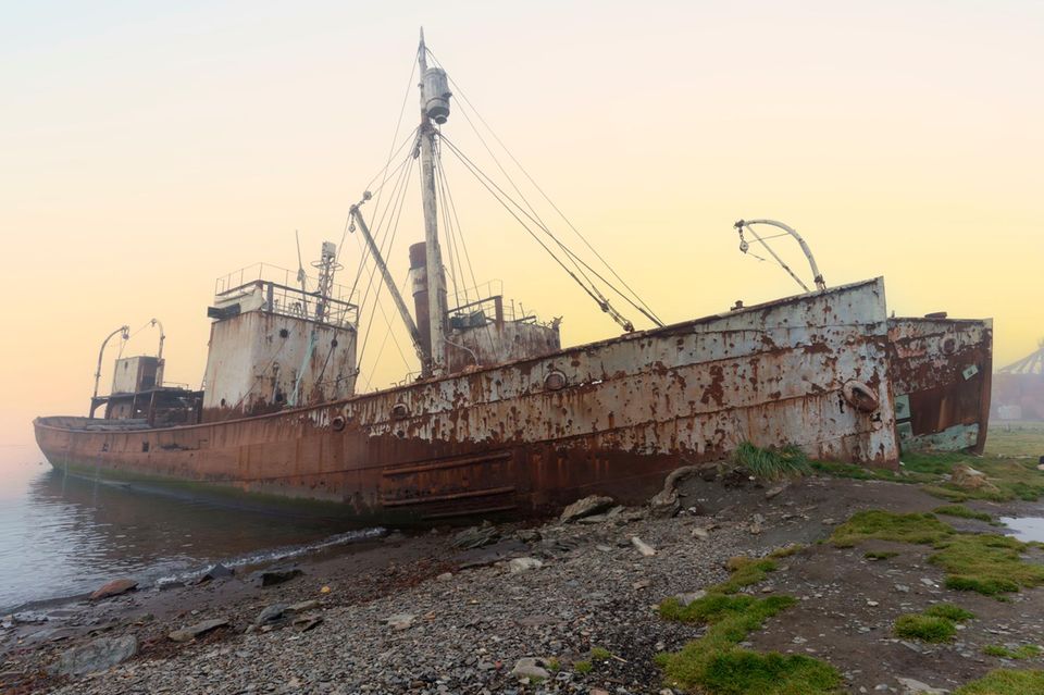 Ein nach und nach rostendes Schiffswrack an einem Steinstrand