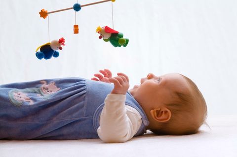 Baby liegt lachend unter einem hölzernen Mobile