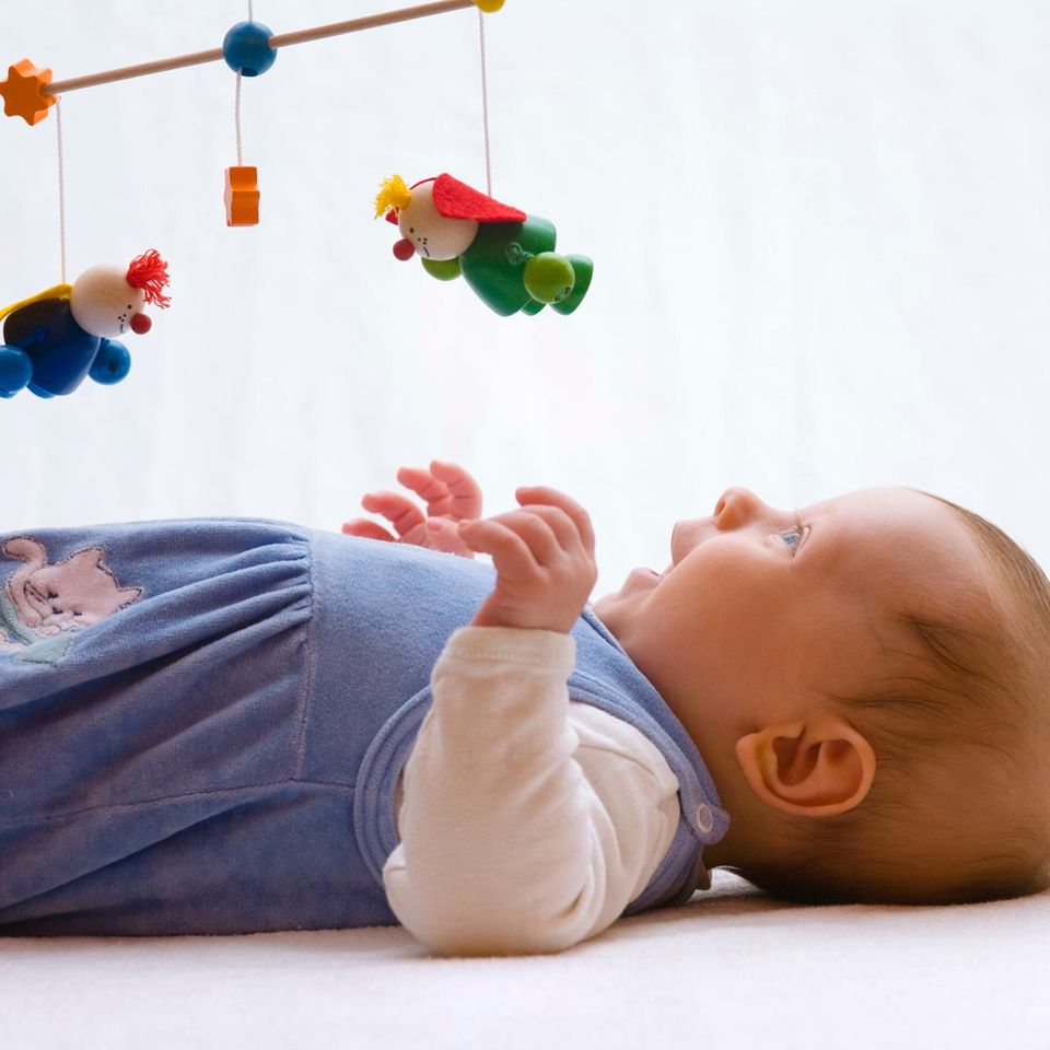 Baby liegt lachend unter einem hölzernen Mobile