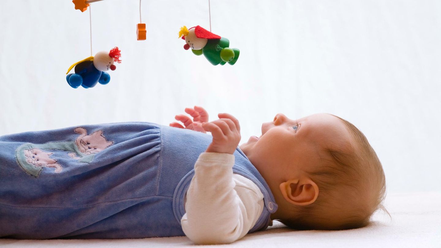 Baby liegt lachend unter einem hölzernen Mobile