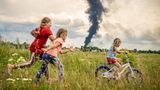 Das Unicef-Foto des Jahres rückt kindliche Unbeschwertheit inmitten des russischen Angriffskriegs gegen die Ukraine in den Mittelpunkt. Auf dem Siegerbild des polnischen Fotografen Patryk Jaracz sind drei Mädchen auf einer Wiese in der Westukraine zu sehen. Eines davon lernt das Fahrradfahren, während im Hintergrund eine schwarze Rauchwolke von einem Öllager aufsteigt. Die Siegerfotos wurden am Donnerstag in Berlin präsentiert.  Jaracz habe eine "sehr bewegende Szene mit einem sehr beklemmenden Kontrast festgehalten", sagte Unicef-Schirmherrin Elke Büdenbender, die Frau des Bundespräsidenten Frank-Walter Steinmeier. "Der Krieg hängt wie eine richtig dunkle Wolke über dem Alltag der Kinder." Trotzdem zeige es auch Hoffnung.