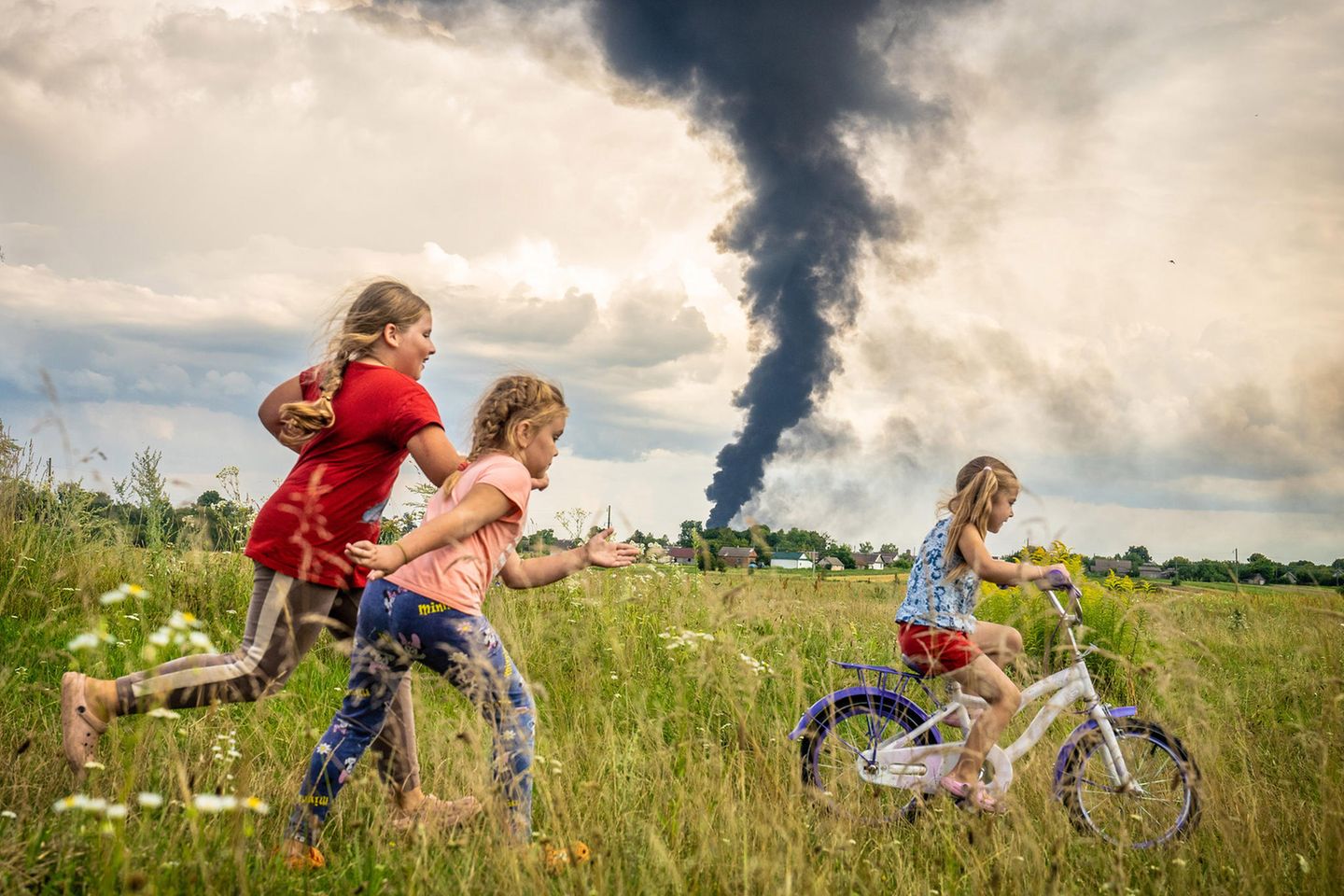 Erster Preis: Patryk Jaracz Das Unicef-Foto des Jahres rückt kindliche Unbeschwertheit inmitten des russischen Angriffskriegs gegen die Ukraine in den Mittelpunkt. Auf dem Siegerbild des polnischen Fotografen Patryk Jaracz sind drei Mädchen auf einer Wiese in der Westukraine zu sehen. Eines davon lernt das Fahrradfahren, während im Hintergrund eine schwarze Rauchwolke von einem Öllager aufsteigt. Die Siegerfotos wurden am Donnerstag in Berlin präsentiert. Jaracz habe eine "sehr bewegende Szene mit einem sehr beklemmenden Kontrast festgehalten", sagte Unicef-Schirmherrin Elke Büdenbender, die Frau des Bundespräsidenten Frank-Walter Steinmeier. "Der Krieg hängt wie eine richtig dunkle Wolke über dem Alltag der Kinder." Trotzdem zeige es auch Hoffnung.