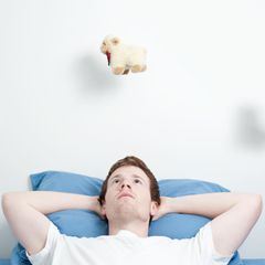 Mann liegt wach im Bett und zählt Schäfchen